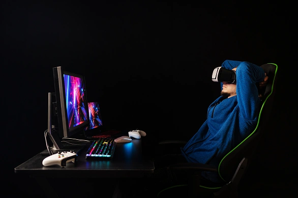 Homem com óculos VR descansa numa cadeira gaming junto a uma secretária com teclado iluminado e comandos